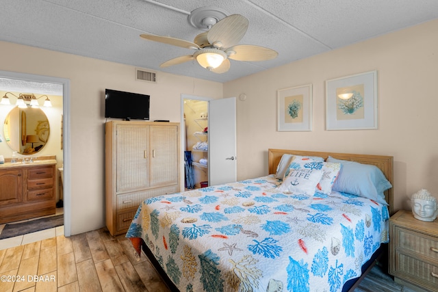 bedroom with a textured ceiling, hardwood / wood-style flooring, ceiling fan, and connected bathroom