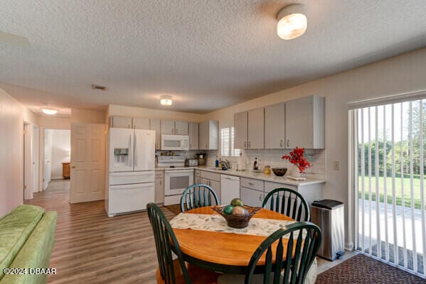 kitchen with decorative backsplash, white appliances, a textured ceiling, and light hardwood / wood-style flooring