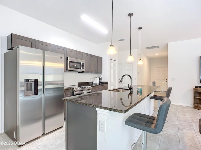 kitchen with sink, decorative light fixtures, a center island with sink, dark stone counters, and stainless steel appliances