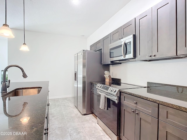 kitchen with sink, decorative light fixtures, light tile patterned floors, dark stone countertops, and stainless steel appliances