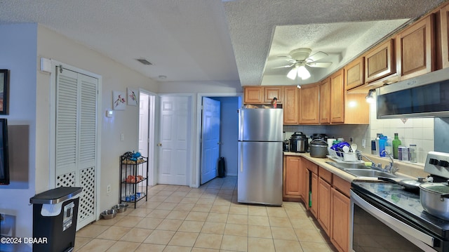 kitchen with appliances with stainless steel finishes, a textured ceiling, decorative backsplash, sink, and ceiling fan