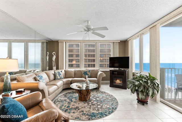 living area featuring light tile patterned floors, a textured ceiling, ceiling fan, a wall of windows, and a glass covered fireplace