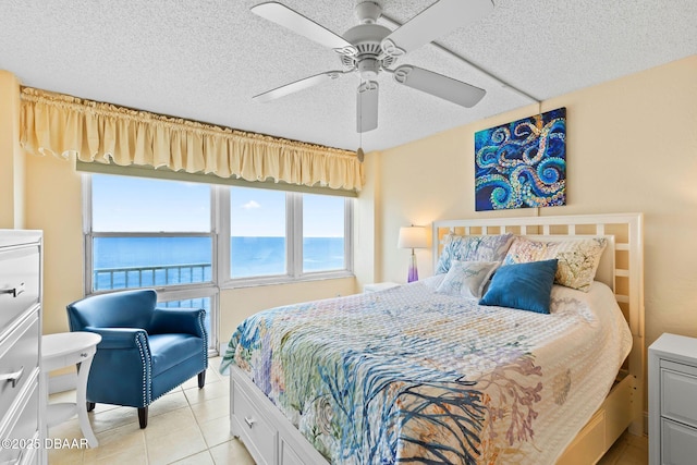 bedroom with a textured ceiling, a water view, light tile patterned flooring, and a ceiling fan