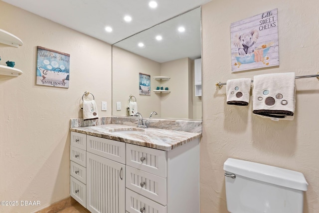 bathroom with toilet, a textured wall, recessed lighting, and vanity