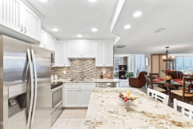 kitchen featuring light tile patterned floors, white cabinets, appliances with stainless steel finishes, light stone counters, and decorative light fixtures