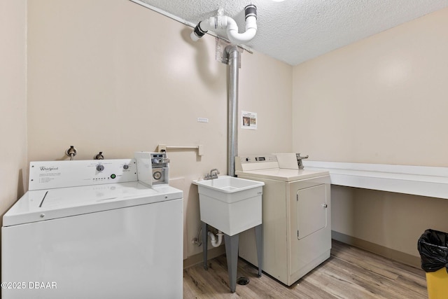 clothes washing area featuring light wood finished floors, a textured ceiling, washer and clothes dryer, and a sink