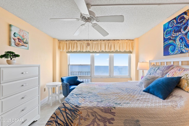 bedroom featuring light tile patterned floors, a water view, ceiling fan, a textured ceiling, and baseboards