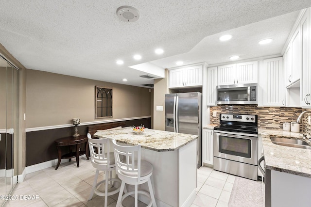 kitchen featuring light stone counters, a center island, appliances with stainless steel finishes, white cabinets, and a sink