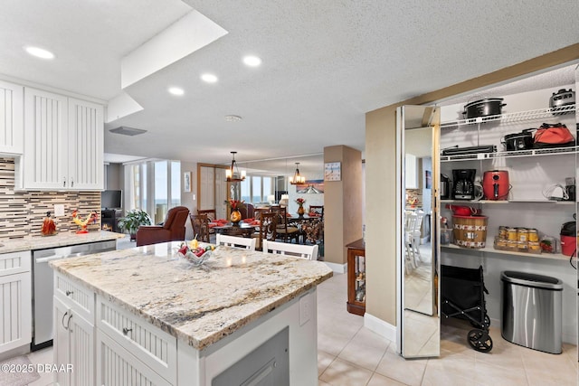 kitchen featuring a center island, white cabinetry, stainless steel dishwasher, and an inviting chandelier