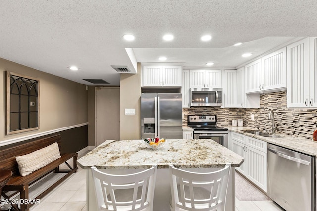 kitchen with light stone counters, stainless steel appliances, a breakfast bar, visible vents, and a center island