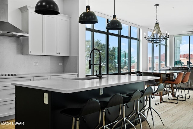 kitchen with wall chimney exhaust hood, sink, plenty of natural light, and a center island with sink