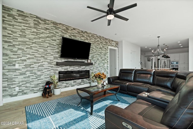 living room with ceiling fan with notable chandelier, a large fireplace, and light hardwood / wood-style flooring