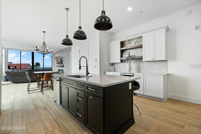 kitchen with sink, backsplash, white cabinets, and an island with sink