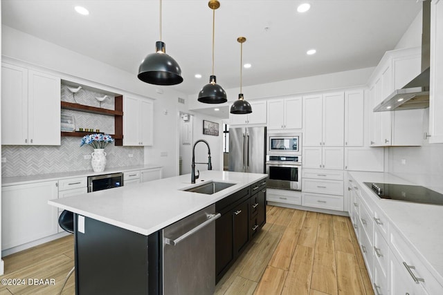 kitchen featuring white cabinets, wall chimney exhaust hood, decorative light fixtures, stainless steel appliances, and a center island with sink