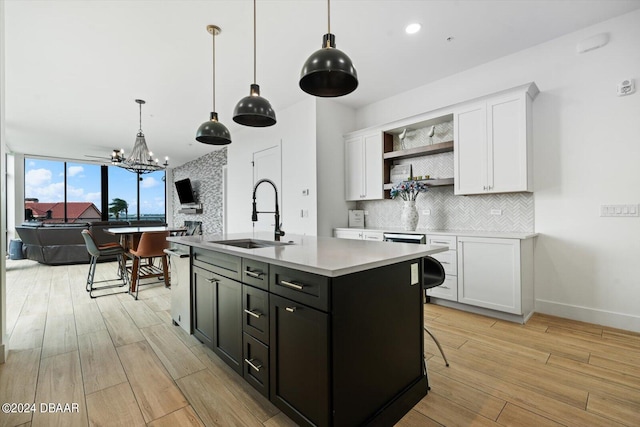 kitchen featuring hanging light fixtures, a kitchen island with sink, sink, and white cabinetry