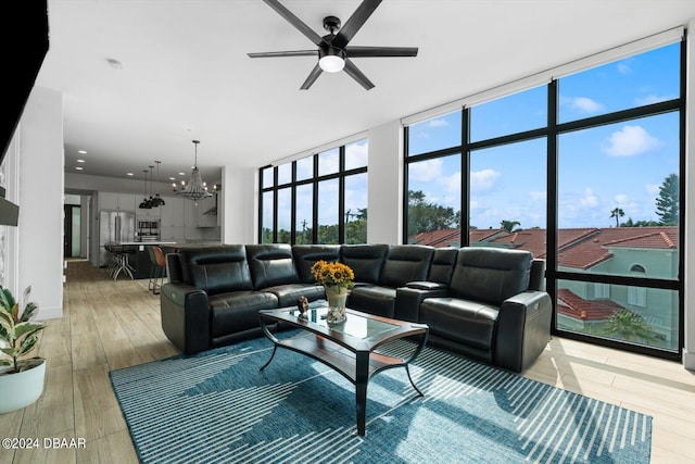 living room with ceiling fan with notable chandelier, light hardwood / wood-style flooring, and expansive windows