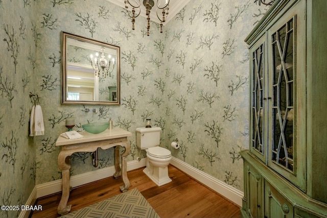 half bath featuring toilet, an inviting chandelier, wood finished floors, baseboards, and wallpapered walls