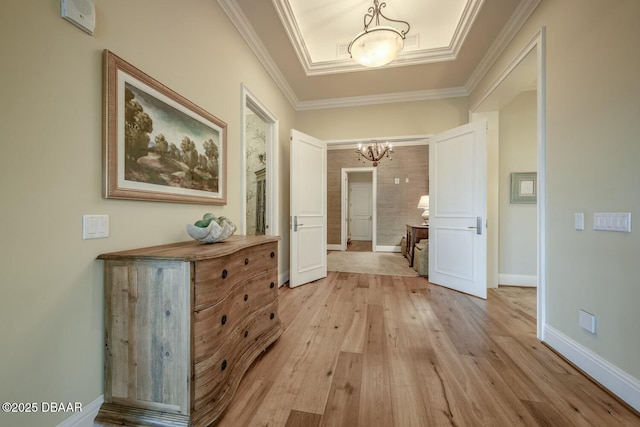 corridor with light wood-style floors, a notable chandelier, crown molding, and baseboards