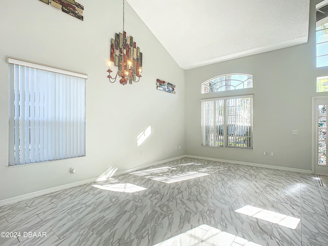 spare room featuring high vaulted ceiling, a healthy amount of sunlight, a textured ceiling, and a notable chandelier