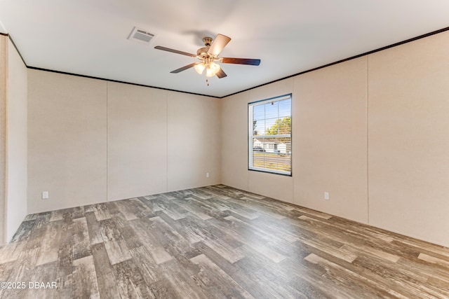 empty room with wood finished floors, a ceiling fan, and crown molding