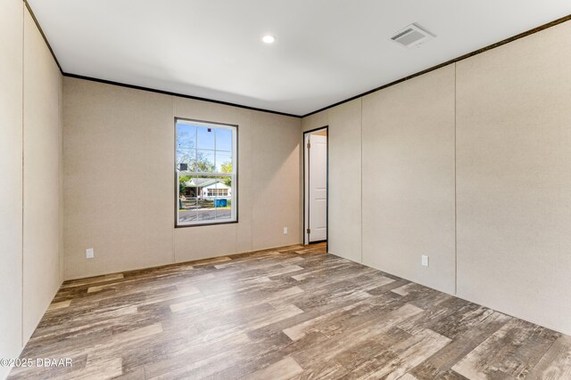 spare room with visible vents, wood finished floors, and ornamental molding