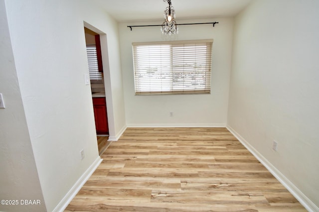 empty room with a notable chandelier and light wood-type flooring