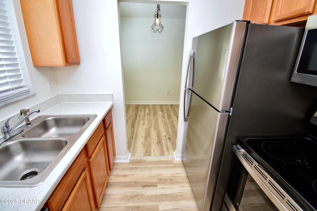 kitchen with stainless steel appliances, sink, decorative light fixtures, and light hardwood / wood-style floors