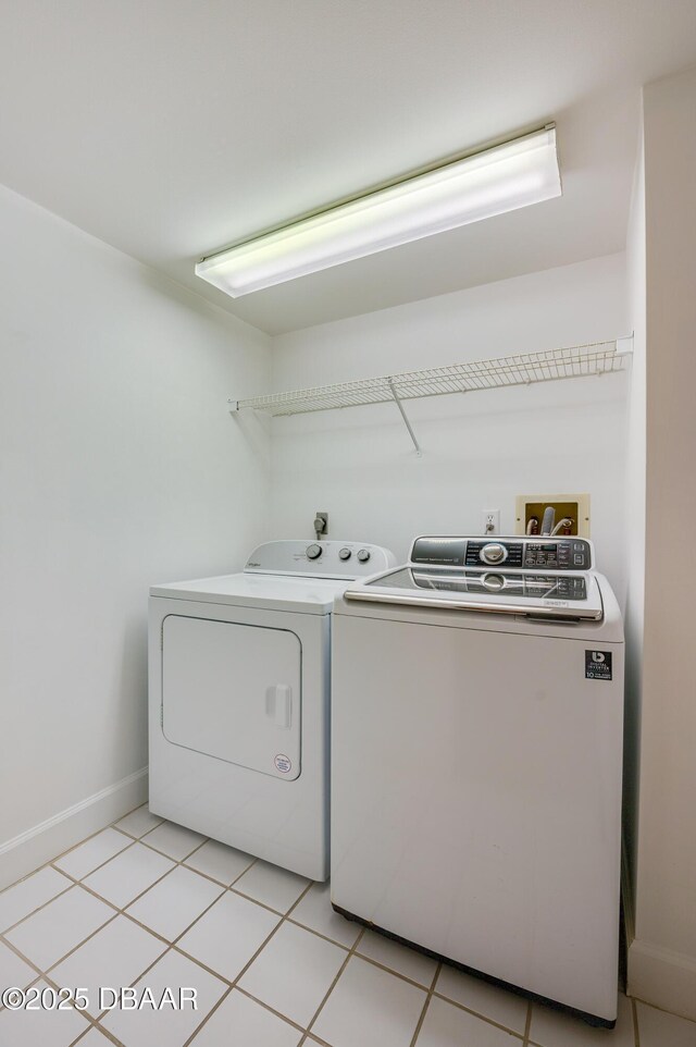 clothes washing area featuring laundry area, light tile patterned floors, baseboards, and washing machine and clothes dryer