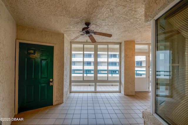 interior space with light tile patterned floors, ceiling fan, and a textured wall