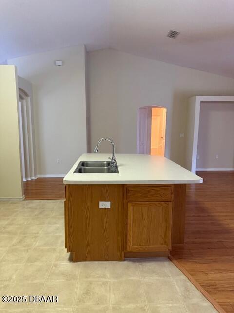 107 Beacon Mill Ln, Palm Coast, FL 32137 - kitchen with light countertops, a kitchen island with sink, light wood finished floors, brown cabinets, and vaulted ceiling