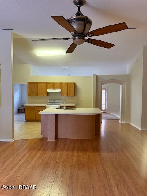 107 Beacon Mill Ln, Palm Coast, FL 32137 - kitchen featuring light countertops, light wood-style flooring, arched walkways, a center island with sink, and range