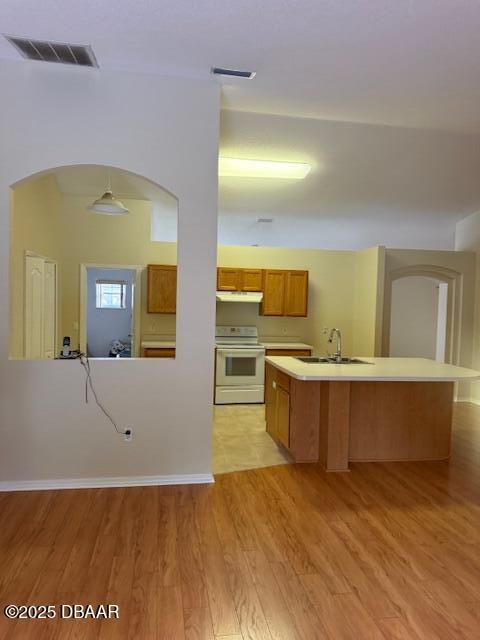 107 Beacon Mill Ln, Palm Coast, FL 32137 - kitchen with white electric range oven, brown cabinetry, arched walkways, light wood finished floors, and a kitchen island with sink