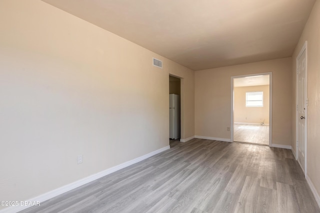 unfurnished room with light wood-type flooring, visible vents, and baseboards