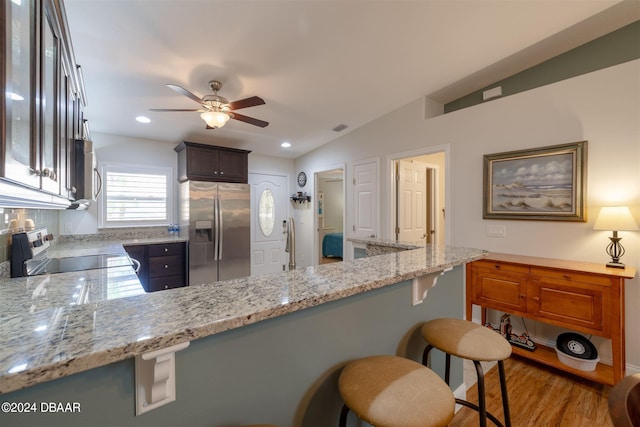 kitchen with lofted ceiling, hardwood / wood-style floors, light stone counters, and stainless steel appliances