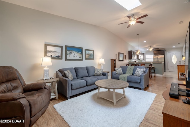 living room with light hardwood / wood-style flooring, ceiling fan, and vaulted ceiling with skylight