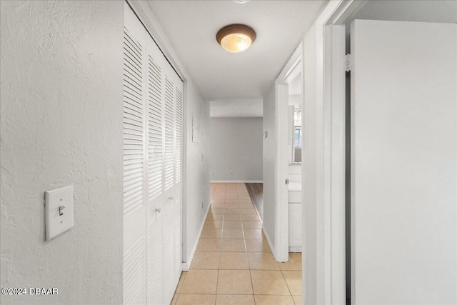 hallway featuring light tile patterned floors, baseboards, and a textured wall