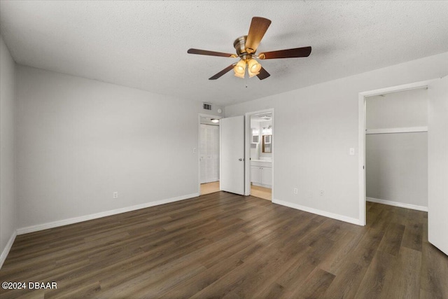 unfurnished bedroom with a closet, a spacious closet, ensuite bath, dark hardwood / wood-style flooring, and ceiling fan