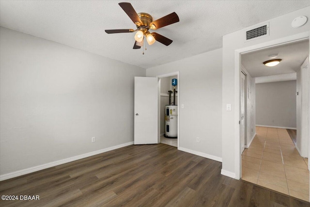 unfurnished bedroom featuring wood finished floors, baseboards, visible vents, a textured ceiling, and electric water heater