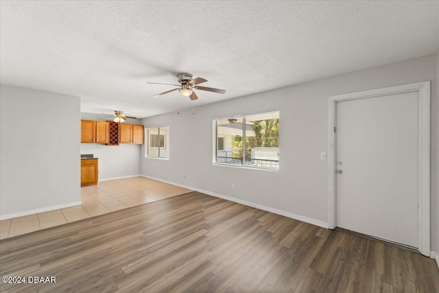 unfurnished living room featuring a textured ceiling, light wood-type flooring, and ceiling fan