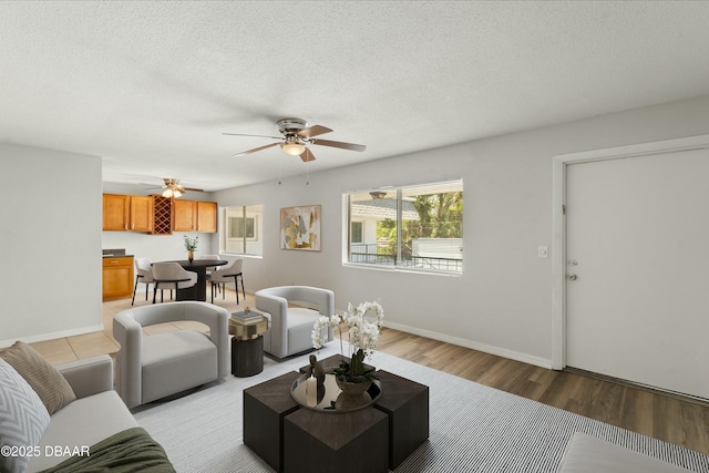 living room with a ceiling fan, light wood-style floors, baseboards, and a textured ceiling