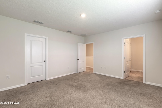 unfurnished bedroom featuring light colored carpet, ensuite bath, and a textured ceiling