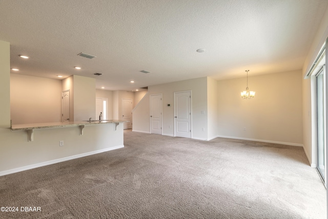 unfurnished living room with carpet, a textured ceiling, and an inviting chandelier