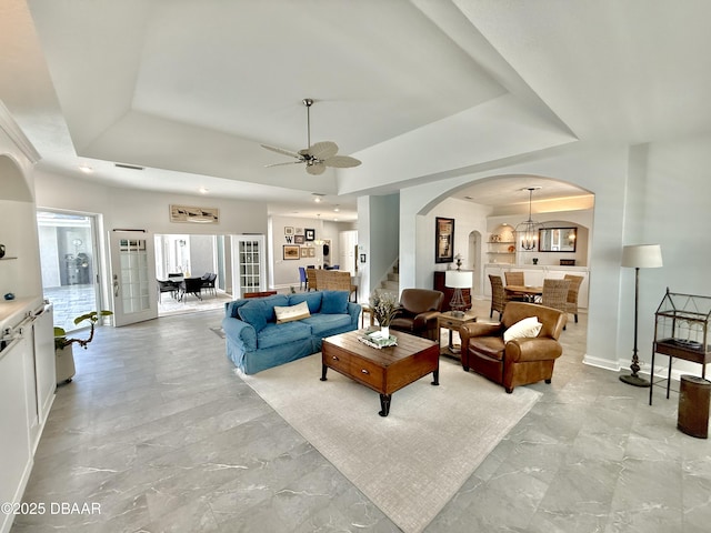1811 N Central Ave, Flagler Beach, FL 32136 - living room featuring stairs, baseboards, a tray ceiling, arched walkways, and ceiling fan with notable chandelier
