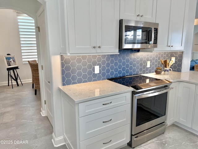 1811 N Central Ave, Flagler Beach, FL 32136 - kitchen with decorative backsplash, white cabinetry, light stone counters, arched walkways, and stainless steel appliances