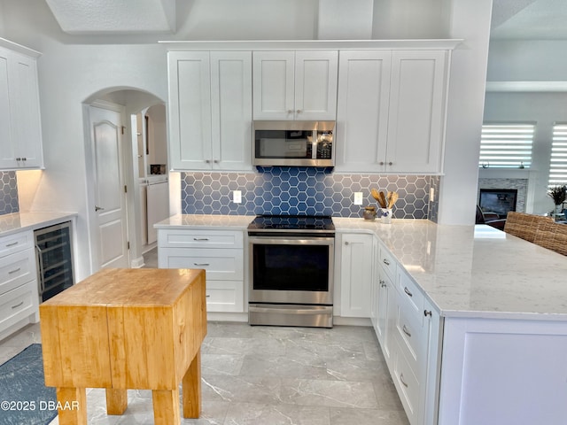 1811 N Central Ave, Flagler Beach, FL 32136 - kitchen featuring beverage cooler, white cabinetry, tasteful backsplash, arched walkways, and stainless steel appliances