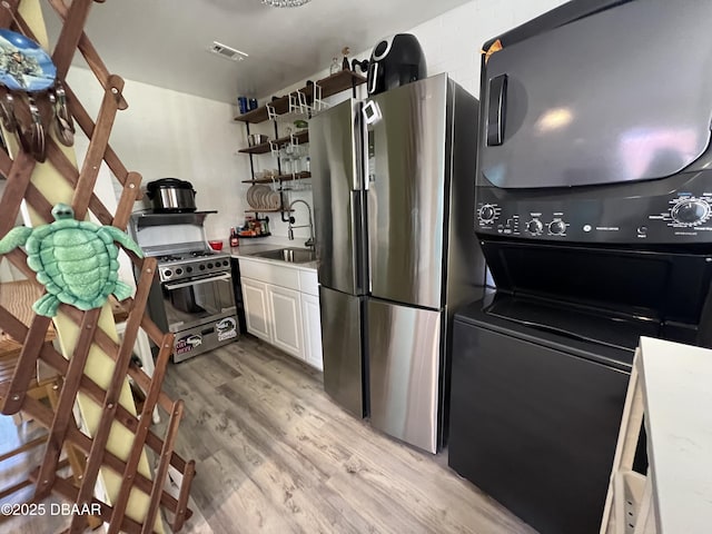 kitchen featuring light wood finished floors, a sink, appliances with stainless steel finishes, stacked washing maching and dryer, and open shelves