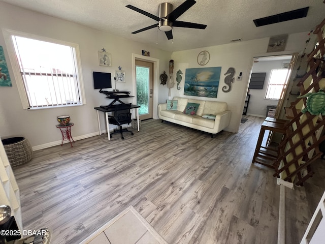 living room with a ceiling fan, baseboards, wood finished floors, visible vents, and a textured ceiling