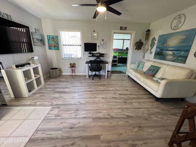 living room featuring ceiling fan, wood finished floors, baseboards, and a textured ceiling