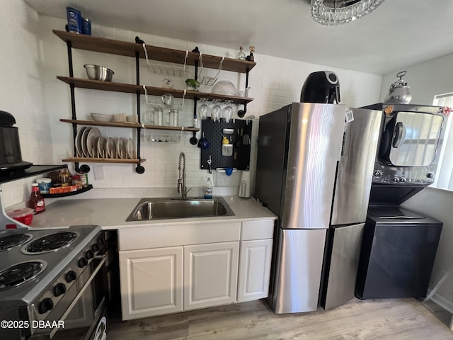 kitchen with light wood finished floors, a sink, stacked washer and clothes dryer, electric range, and open shelves