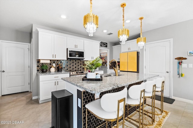 kitchen with pendant lighting, an island with sink, white cabinets, fridge, and light stone countertops